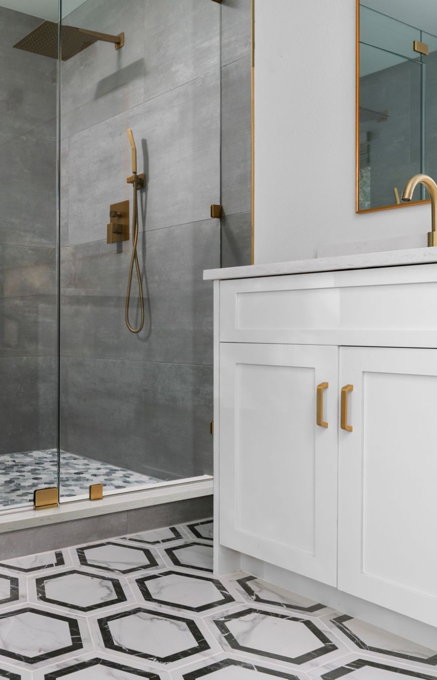A stylish and contemporary bathroom featuring a shower with sleek grey tiles contrasted beautifully with gold fixtures that add a touch of luxury. The white bathroom vanity provides a clean and modern focal point, complemented by decorative white and grey tiles that enhance the space with a subtle pattern.