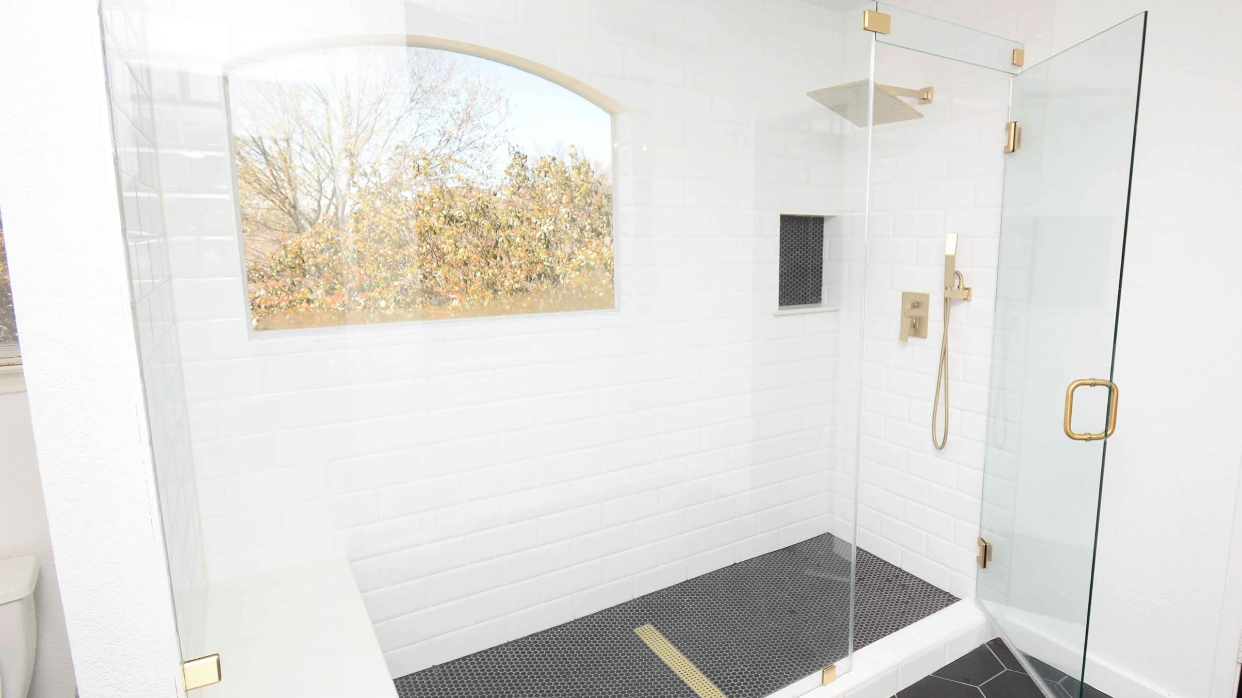 Bright white shower with black tiled floor and gold fixtures